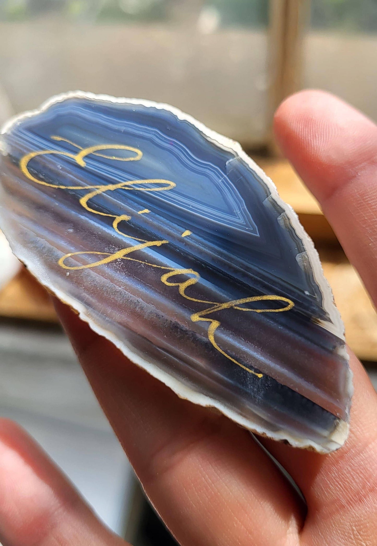A close-up image of a person's hand holding a piece of rock with the word "Ejal" written on it.